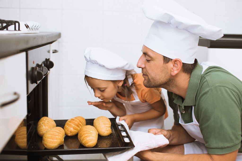 father with daughter  take some rolls on a baking tray  out of oven